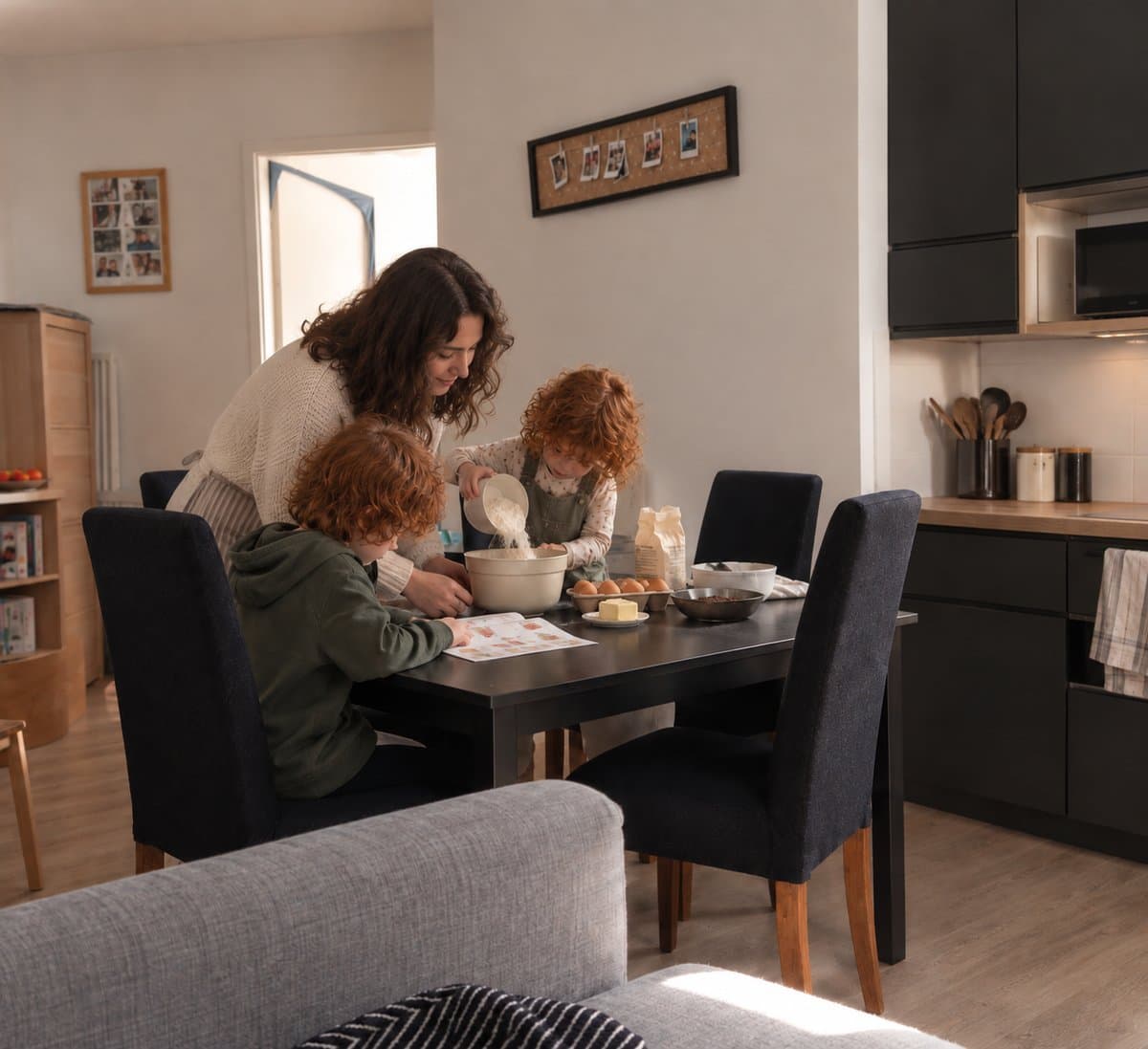 Une maman et ses deux enfants versent la farine dans un saladier, la fiche recette posée sur la table